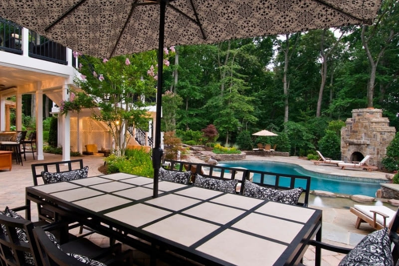 Outdoor Living Area Oasis with Pool and Several Seating Areas Under Enclosed Porch with Outdoor Stone Fireplace | Denny + Gardner Outdoor Living Space Services